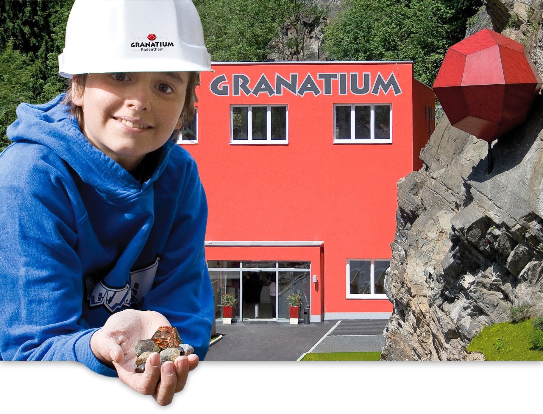 granatium2s-chris_1 Ein Kind mit Helm lacht in die Kamera. Im Hintergrund das Haus Granatium.