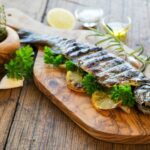 Ein gegrillter Fisch, schön dekoriert mit Zitronen und Petersilie, liegt auf einem Holzbrett.