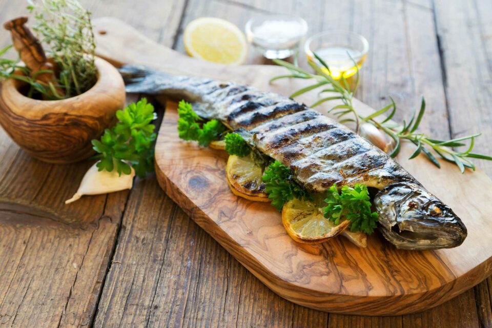 Ein gegrillter Fisch, schön dekoriert mit Zitronen und Petersilie, liegt auf einem Holzbrett.