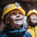 Kinder mit gelben Helm am Kopf stehen im Granatstollen, lächeln und schauen auf die Decke.