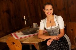 Eine Frau sitzt auf einem Holzstuhl und lächelt. Sie trägt ein Dirndl, eine Granatkette und zwei Granatsteinringe.