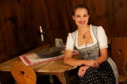 Eine Frau sitzt auf einem Holzstuhl und lächelt. Sie trägt ein Dirndl, eine Granatkette und zwei Granatsteinringe.