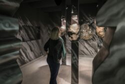 Eine Frau sieht sich in der Ausstellung im Granatmuseum einen großen, grauen Granatstein mit schwarzen Strichen an.