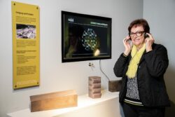 Eine ältere Dame hört per Audioguide der Sonderausstellung das Werk zu.
