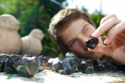 Ein Junge hält einen weinroten kleinen Granatstein in der Hand und sieht mit einem Auge zu ihm.