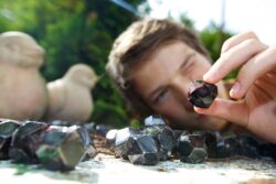 Ein Junge hält einen weinroten kleinen Granatstein in der Hand und sieht mit einem Auge zu ihm.